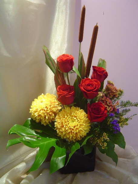 Roses, commercial mums, cattails, celosia, waxflowers, statice, monstera, and cordeline