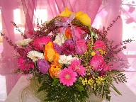 Yellow calla lillies, heather, gerbera, hot pink roses, mimosa, and tulips in a basket arrangement