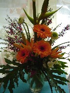 Gerberas, heliconia, ranunclus, boronia, pink and white orchids, asiatic lilies, and philodendron leaves in a vase
